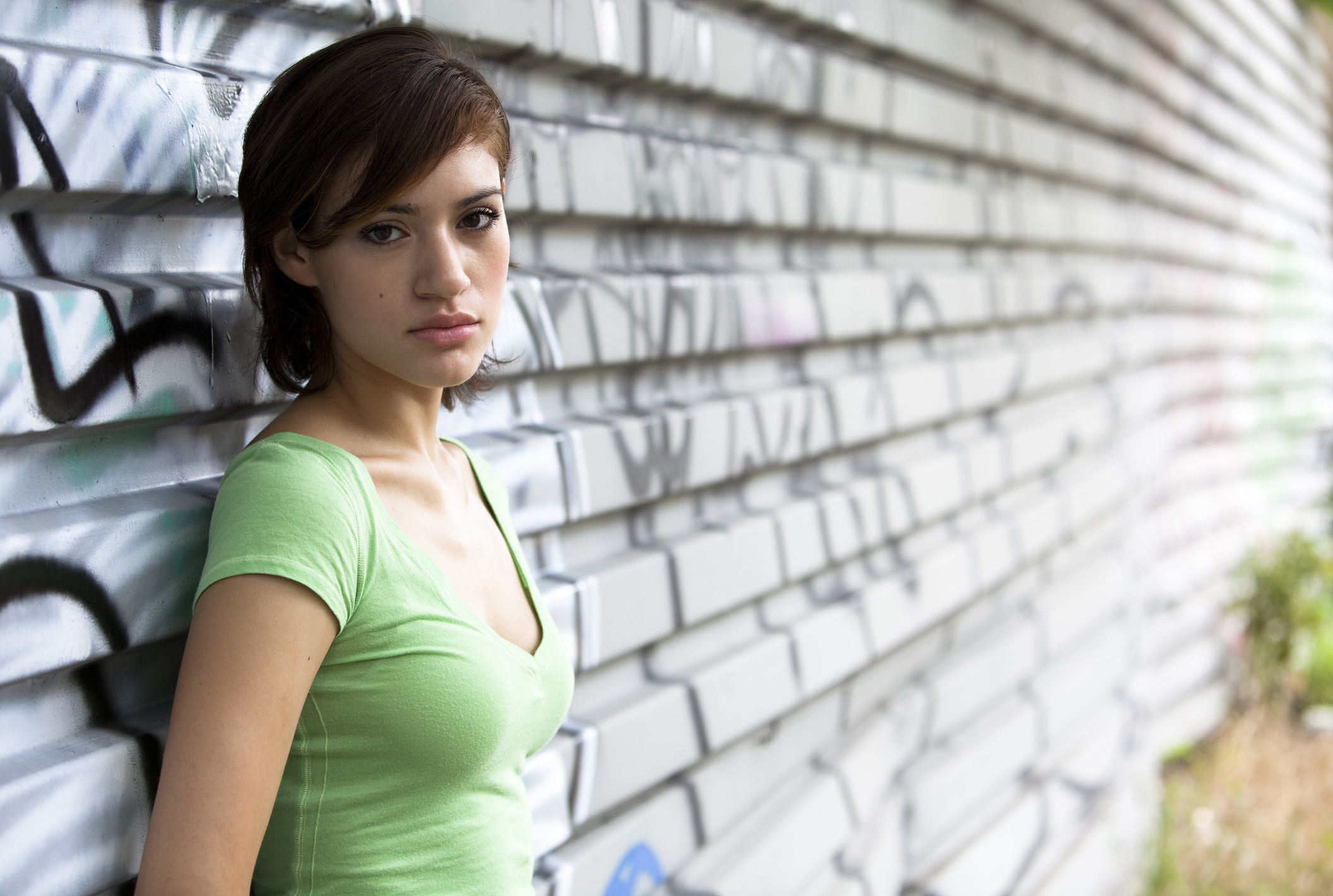 Young female standing against a tin fence covered with graffiti.